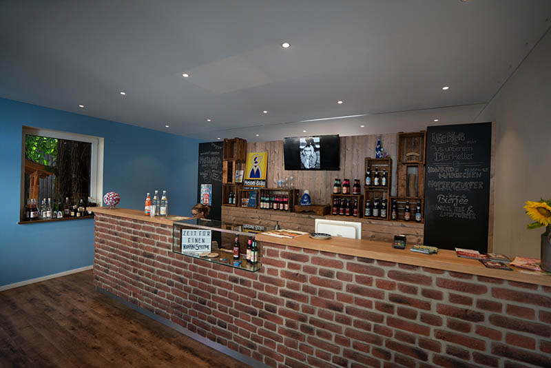 Ein Verkaufsraum mit geklinkerter Theke, dahinter verschiedene Bierflaschen auf Wandregalen.